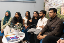 A group of young people from different backgrounds, dressed casually. They are sitting on a sofa. They are looking straight ahead. There is a table in front of them.