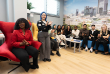 A group of young people from different backgrounds, dressed casually. Most are sitting, one is standing. Behind them, on the wall, there is a photo wallpaper of the Medical University of Warsaw campus.