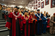 A group of people during a ceremony. They are wearing academic gowns. They are smiling for the camera. 