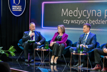 Trzy osoby siedzą na scenie podczas panelu dyskusyjnego. Mężczyzna po lewej, prorektor ds. nauki i transferu technologii trzyma mikrofon i notatnik. Wszyscy uczestniczą w rozmowie. W tle widać napis „Medycyna przyszłości – czy wszyscy będziemy zdrowi?”.