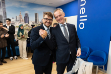 The vice dean and dean pose for a photo, smiling. Their right hands are clasped together. Behind them, other participants in the official opening can be seen.