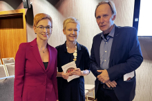 Three elegantly dressed people: two women and one man pose for a photo. They are smiling.
