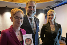 Three people: two women and a man pose for a photo. They are smiling. One of the women is holding a book dedicated to Prof. Kossakowski.