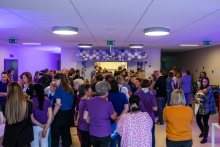 Grupa osób, ubranych w większości w fioletowe koszulki, w szpitalnym pomieszczeniu. Pomieszczenie jest podświetlone na fioletowo.