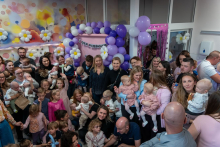 A group of people posing for a photo. Everyone is smiling. Behind them, you can see purple balloons, and there are colorful drawings on the walls.