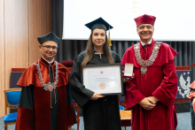 On the left is the dean, in the center the top graduate holding a framed diploma, and on the right the vice-rector. They are all posing for the photo.