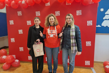 Three women posing for a photo in front of a red backdrop with the white logo of Szlachetna Paczka.