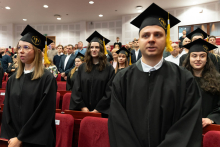 A group of graduates, wearing black caps and gowns, is taking an oath. They are all standing.