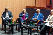 Five people are sitting in armchairs during a discussion. One of them is holding a microphone and speaking.