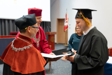 A young man is receiving a diploma from the dean and the vice-rector.