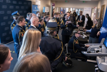 A group of police officers is standing by an exhibition booth where a woman is presenting medical or technological equipment. In the background, banners and other trade fair stands are visible.
