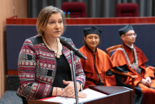A smartly dressed woman is speaking from behind the lectern. Next to her are the dean and the vice-dean for education in the medical analytics program, seated.