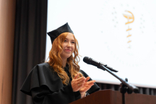 A young woman, Sabina Sobolewska, dressed in a black gown, is standing behind the lectern, smiling and clapping.