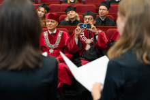 Guests of the ceremony seated in the auditorium. In the foreground, from behind, the performing choir is visible. One of the seated guests is taking a photo of them.