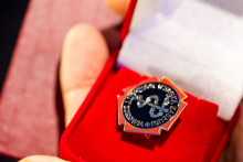 A close-up of a hand holding an open red box containing a star-shaped badge with a black circular center and silver lettering.