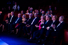 A group of people in formal attire is seated in an auditorium during an event.