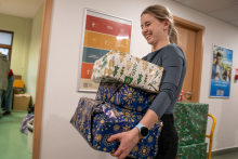 A young girl carrying three packages wrapped in white and blue paper.