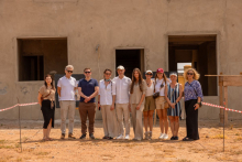 A group of people is standing outside in front of an unfinished building under construction, with warning tape markings visible on the ground.
