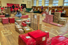 A gymnasium floor covered with numerous wrapped gifts. People can be seen in the background.