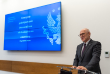 Elegancko ubrany mężczyzna, rektor WUM, stoi za mównicą i przemawia. 