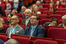 Uczestnicy sympozjum, siedzą na czerwonych fotelach.