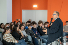 Prof. Czupryniak w czasie wykładu stoi na środku sali i przemawia do mikrofonu. Przed nim w rzędach siedzą młodzi ludzie.