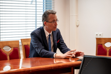 A man during a meeting. He is elegantly dressed. He rests his hands on the table. He is explaining something.