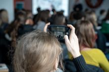 Uczestnicy wykładu, na pierwszym planie jedna z osób trzyma uniesiony telefon i robi nim zdjęcie.
