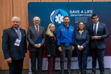 Six people stand in front of a navy blue wall with the inscription “SAVE A LIFE – World Congress of Polish Medical Communities.” The people are dressed elegantly. Six people are standing in front of a navy blue wall with the inscription ‘SAVE A LIFE – World Congress of Polish Medical Communities’. The people are dressed elegantly. Among them, second from the left, is the rector of the Medical University of Warsaw, next to the Minister of Health, and then Sławosz Uznański-Wiśniewski.