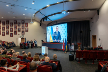 Grupa osób na auli, patrzy na ekran, na którym wyświetlany jest film z udziałem mężczyzny - ministra zdrowia Ukrainy.