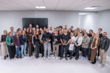 Około czterdzieści osób stoi w dużej sali w kilku rzędach. Trzy osoby na środku trzymają szklane statuetki i dyplomy, co wskazuje na odbiór nagród. Pozostałe osoby stoją obok w eleganckich lub półformalnych strojach. 