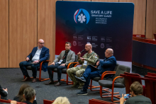 Four men are sitting in a room during a panel discussion. One of them, wearing a military uniform, is holding a microphone. The others are dressed elegantly. The first person on the right is Prof. Robert Gałązkowski.