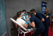 Mężczyzna siedzi odchylony na fotelu zabiegowym, a trzy kobiety w medycznych uniformach pochylają się nad nim, wykonując przegląd jamy ustnej przy użyciu latarki i narzędzi stomatologicznych.