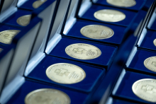 Rzędy otwartych pudełek prezentują medale ułożone w uporządkowanych liniach. Każdy medal leży w wyściółce i pokazuje grawer z nazwą uczelni.