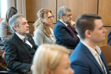 Uczestnicy konferencji, którzy siedzą na krzesłach i patrzą przed siebie.