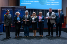 Kilka elegancko ubranych osób pozuje do zdjęcia. W tle widać ekran multimedialny oraz rollupy.