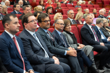 Participants of the event are seated in the red auditorium chairs, attentively listening to the ceremony program