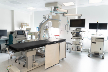 Fully equipped medical procedure room with an examination table, imaging equipment, monitors, and various diagnostic and surgical devices arranged around the space.