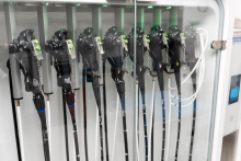 A row of medical endoscopes stored vertically inside a glass cabinet, each secured in place with holders and illuminated by small indicator lights.