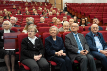 Participants of the event are seated in the red armchairs of the large auditorium, forming several rows of the audience during the ceremony.