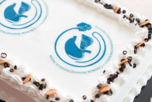 Decorated cake featuring a printed medical logo with a stylized stomach and liver, surrounded by piped white frosting and chocolate decorations.