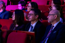 Three people are sitting in a row and looking toward the stage. Their posture is calm, with their hands resting naturally on their knees or on the armrests. They are all focused on the performance.