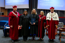 Five people stand together during the ceremony. The graduate in an academic gown stands in the middle holding a document. On both sides of her stand the vice‑rectors and the chair of the disciplinary council, all dressed in gowns. All of them are looking toward the photographer.