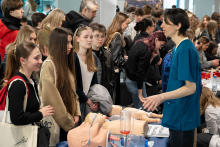 An educational station with medical manikins used for learning emergency procedures, where event participants are listening to the presenter explaining how they work.