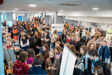 A crowd of participants moving between educational booths during a large indoor event; various stations, anatomical models, and informational materials are visible
