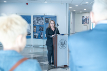A person standing at a lectern during a speech in an exhibition space, surrounded by display boards with archival photographs.