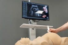 A training station with a medical manikin; a person is applying an ultrasound probe, and simulation ultrasound images are visible on the monitor.