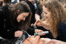 People practicing the intubation procedure on a medical manikin; one person is inserting the endotracheal tube while the other provides guidance, pointing out the correct positioning of the equipment.