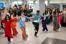 A group of dancers performing a choreography in traditional costumes during an event, dancing in front of a large audience gathered in the lobby area.
