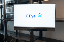 A monitor displaying the C‑Eye system’s welcome screen, placed on a metal shelf in a bright room.